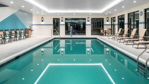 Une grande piscine intérieure à l’eau claire, entourée de chaises longues et d’un espace d’accueil.