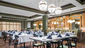 Un restaurant doté de nombreuses tables dressées pour le service, avec un décor intérieur classique comprenant des planchers en bois et des banquettes recouvertes d’un tissu vert.