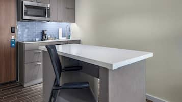 Una cocina moderna con microondas incorporado, cafetera y un lavabo. Hay una encimera blanca y una silla con respaldo.