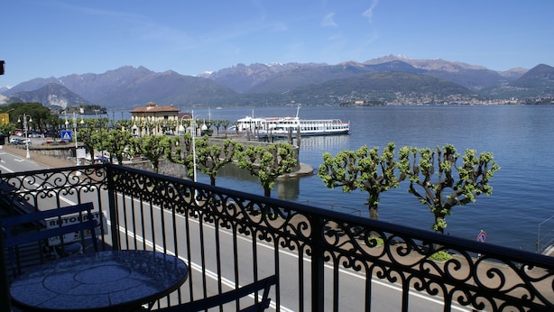 A balcony with a table and chairs overlooking a lake with a boat and mountains in the background. - Lakefront apartment in downtown Stresa with magnificent views (Stresa)