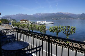 Een balkon met een tafel en stoelen, uitkijkend op een meer met een boot en bergen op de achtergrond.