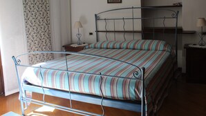 A metal-framed bed with striped bedding in a room with wooden flooring, a nightstand, and a wall-mounted shelf. - Lakefront apartment in downtown Stresa with magnificent views (Stresa)