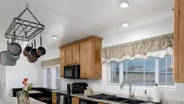 A kitchen with wooden cabinets, a black refrigerator, a microwave, and a hanging pot rack. - Spacious Riverhouse with private park/boat ramp (Parker)