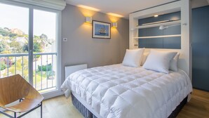 Een slaapkamer met een groot bed, een stoel, uitzicht door een schuifdeur en een lijst met een afbeelding aan de muur.