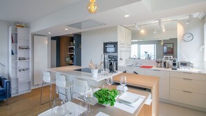 Een moderne keuken met witte kasten, een centraal kookeiland met zitplaatsen, en een eethoek met witte stoelen en een tafel gedekt voor twee personen.