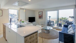 Een moderne keuken met een centraal eiland, witte kasten en een groot raam met uitzicht op zee.