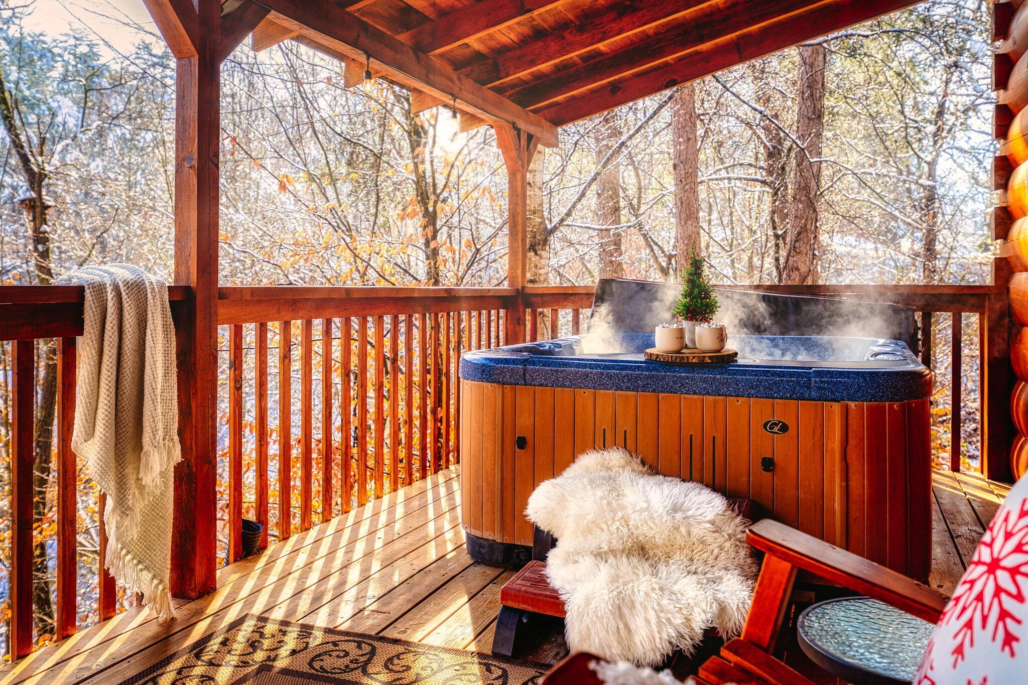 Una terraza de madera con un jacuzzi, un pequeño árbol de Navidad y una alfombra de piel.
