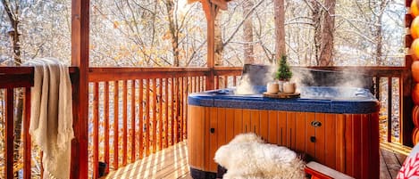 Una terraza de madera con un jacuzzi, un pequeño árbol de Navidad y una alfombra de piel.