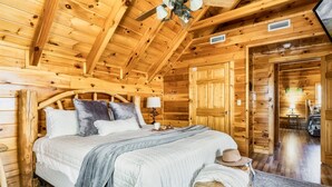 Een slaapkamer in een houten blokhut met een bed, nachtkastje, lamp en een hoed op een kruk.