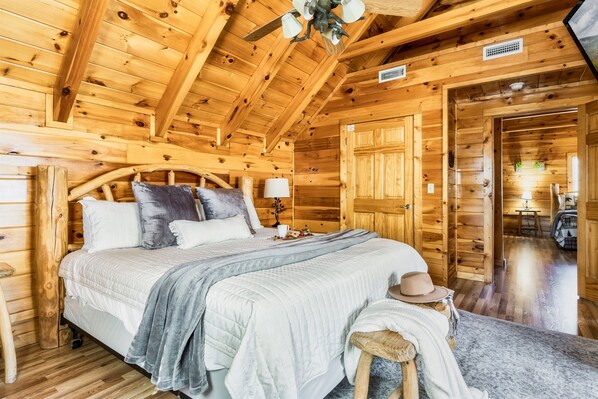 A wooden cabin bedroom with a bed, bedside table, lamp, and a hat on a stool.