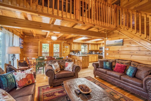 Un intérieur de chalet chaleureux avec des murs et des plafonds en bois, un coin repas, une cuisine et un escalier.
