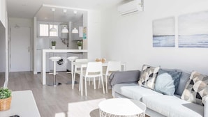 A modern living room with a sofa, dining table, and chairs. There is a kitchen area with white cabinets and a washing machine. - A&n Seafront Torre del Mar (Torre del Mar)