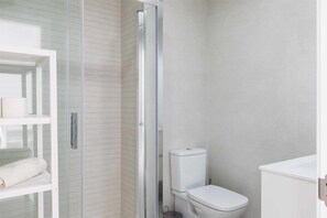 Clean lines and minimalist style define this bathroom, featuring a glass-enclosed shower, white toilet, and sink.