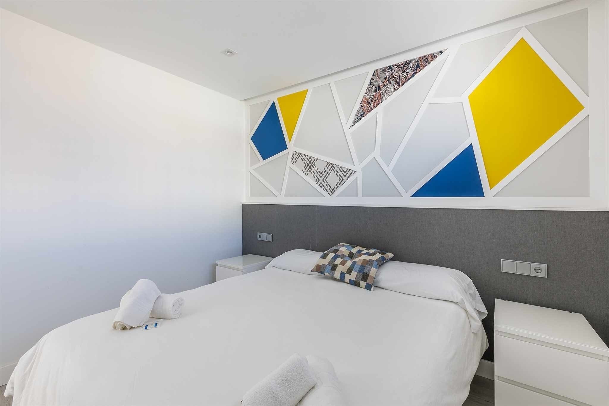 A modern hotel room with a neatly made bed, a bedside table, and a wall with geometric patterns.