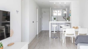A modern kitchen with white cabinets, a dining area with white chairs, and a TV on the left. - A&n Seafront Torre del Mar (Torre del Mar)