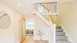 A staircase with wooden steps and white railings, a herringbone-patterned wooden floor, and a dining area with a table and chairs.