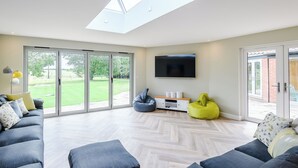 A modern living room with a large TV, sliding glass doors to a garden, and a skylight.