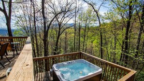 A hot tub on a wooden deck surrounded by trees with a view of mountains.