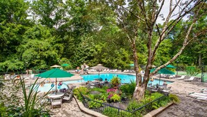 A pool area with lounge chairs and umbrellas, surrounded by lush greenery and trees.