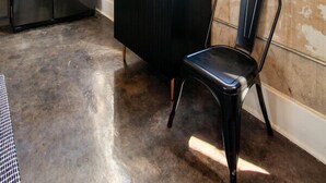 A kitchen with a stainless steel refrigerator, a black countertop, a chair, and large windows with a view of buildings. - Historic Sterchi Loft on Gay St (Knoxville)