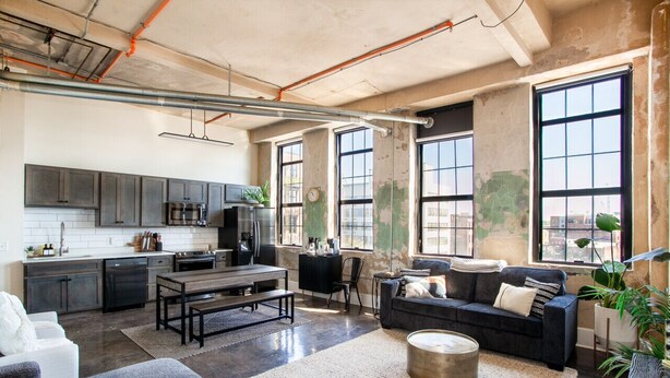 A spacious living area with a kitchen, large windows, and a cozy seating area. - Historic Sterchi Loft on Gay St (Knoxville)