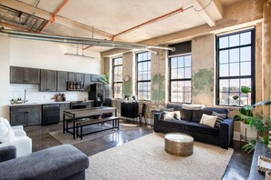 A spacious living area with a kitchen, large windows, and a cozy seating area. - Historic Sterchi Loft on Gay St (Knoxville)