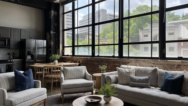 A spacious living room with a large window, a dining area, and a kitchen.