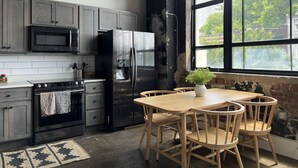 A kitchen with a large window, a wooden dining table, and a refrigerator.