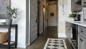 A narrow hallway with a concrete floor, a patterned rug, and a potted plant on a table.