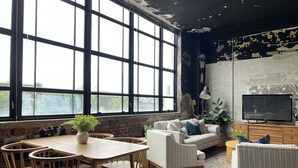 A room with a large window, a sofa, a TV, and a wooden table with chairs.