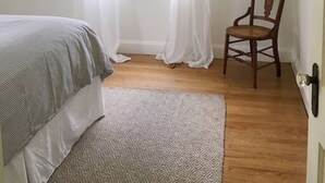 Un dormitorio con cama, una silla, un ventanal con cortinas y una lámpara colgante.