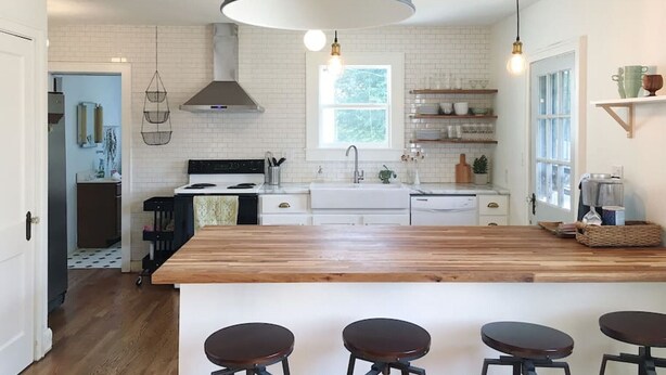 Una cocina moderna con una isla central, taburetes de bar, iluminación colgante y vistas al comedor contiguo.