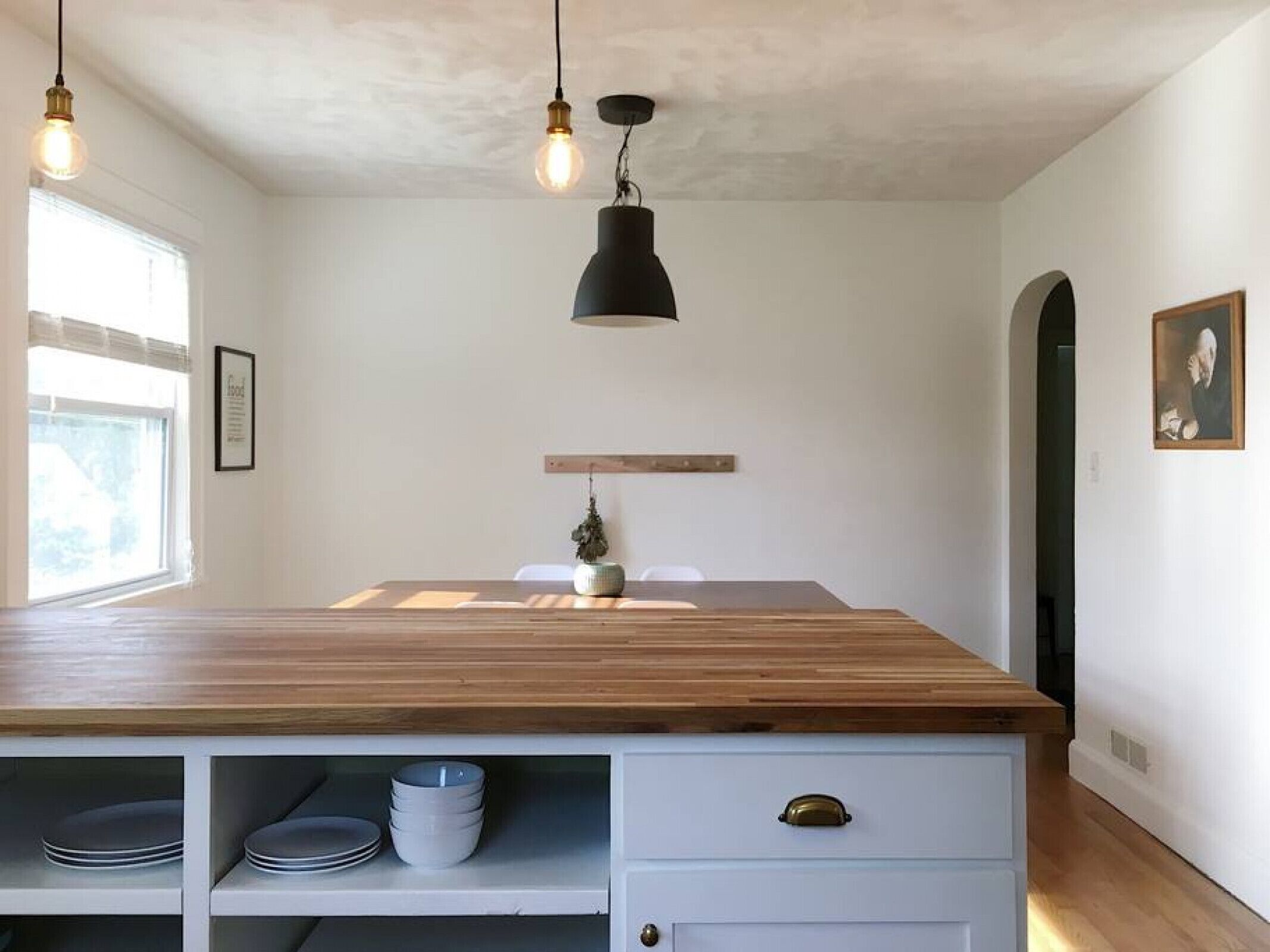 Una cocina con encimera de madera, luces colgantes y un armario blanco con cajones.