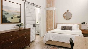 Una camera da letto con un letto, una cassettiera, uno specchio e un quadro appeso al muro.
