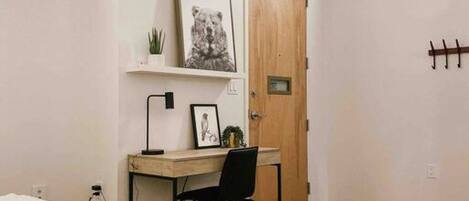 Un dormitorio con cama, escritorio, silla, puerta y perchero en la pared.