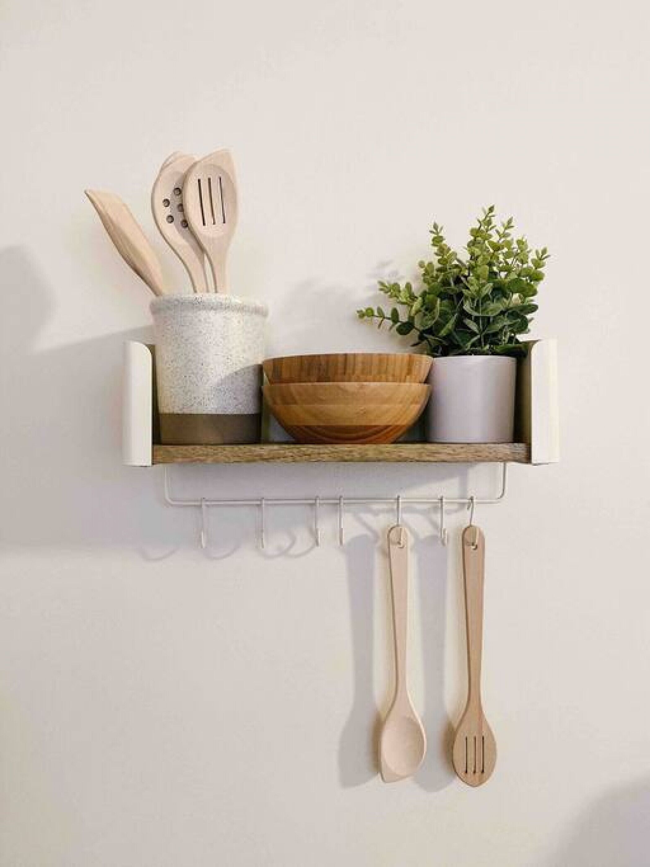 A kitchen shelf with wooden utensils, a bowl, and a potted plant.