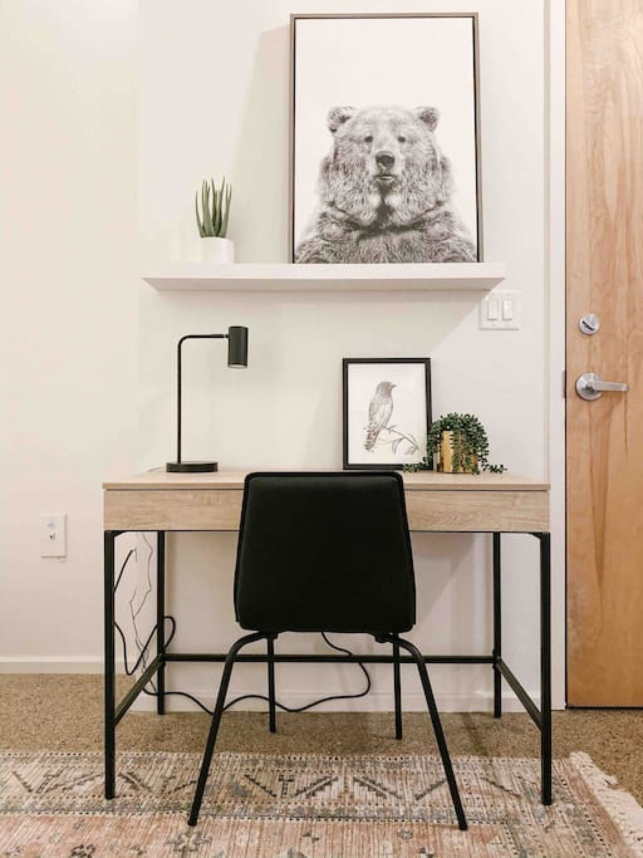 A desk with a black chair, a framed bear picture, a small plant, and a framed bird picture.
