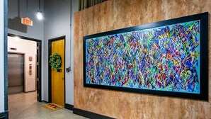 Un corridoio con un grande quadro astratto, un ascensore e una porta decorata con un festone.