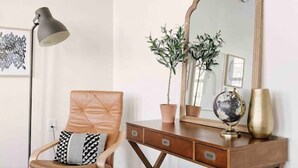 A room with a wooden desk, a chair, a floor lamp, a mirror, a globe, and a vase. - Modern Gay St Loft w/ View (Knoxville)