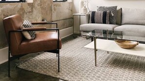 Een woonkamer met een lederen fauteuil, een grijze bank en een salontafel. Er hangen ingelijste foto's aan de muur en een raam met uitzicht.