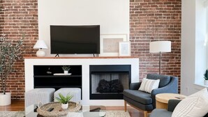 Ein modernes Wohnzimmer mit Backsteinwand, Flachbildfernseher, Kamin und grauem Sofa.