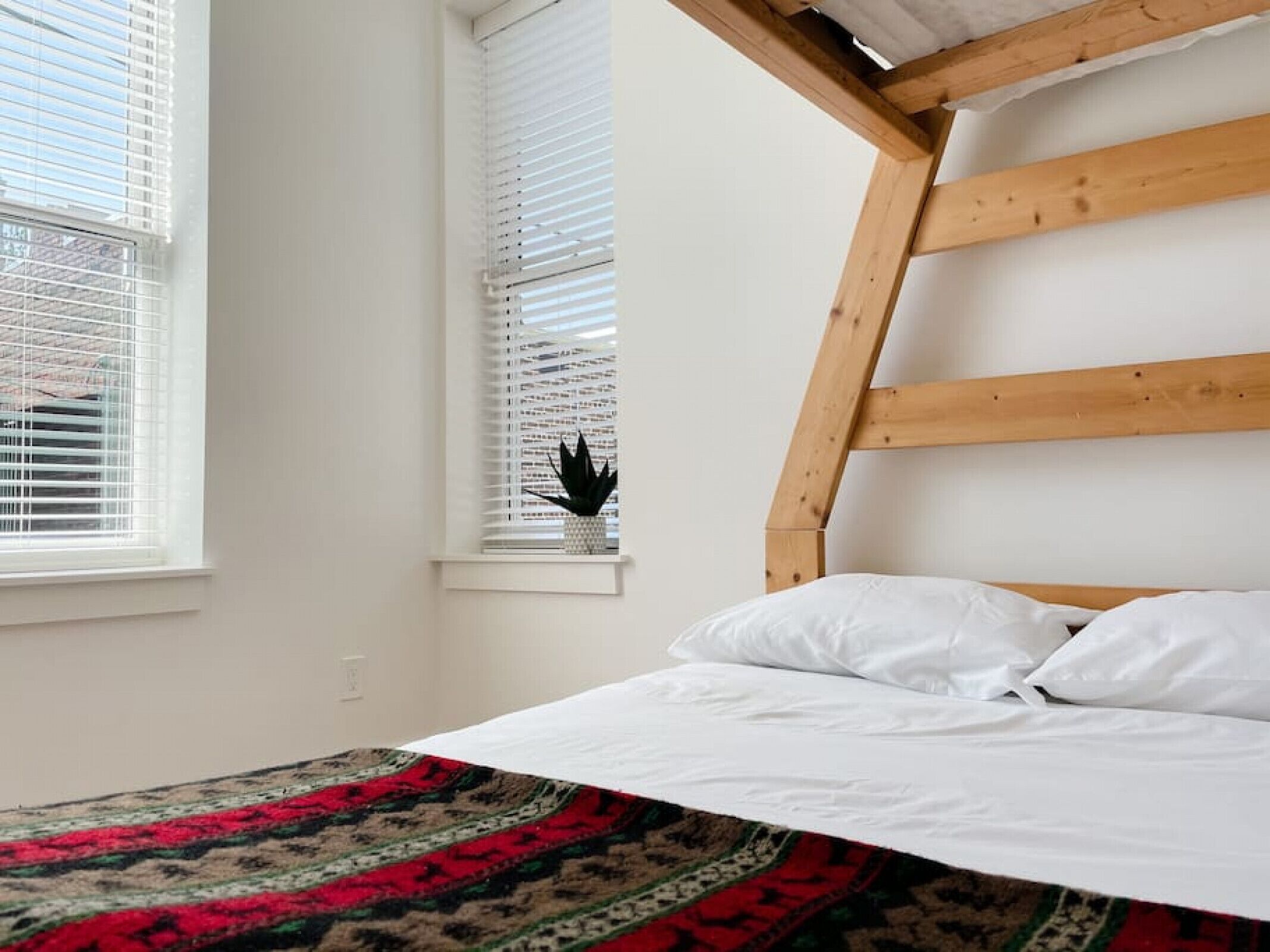 Un dormitorio con cama, ropa de cama blanca, cabecero de madera y una ventana con persianas.