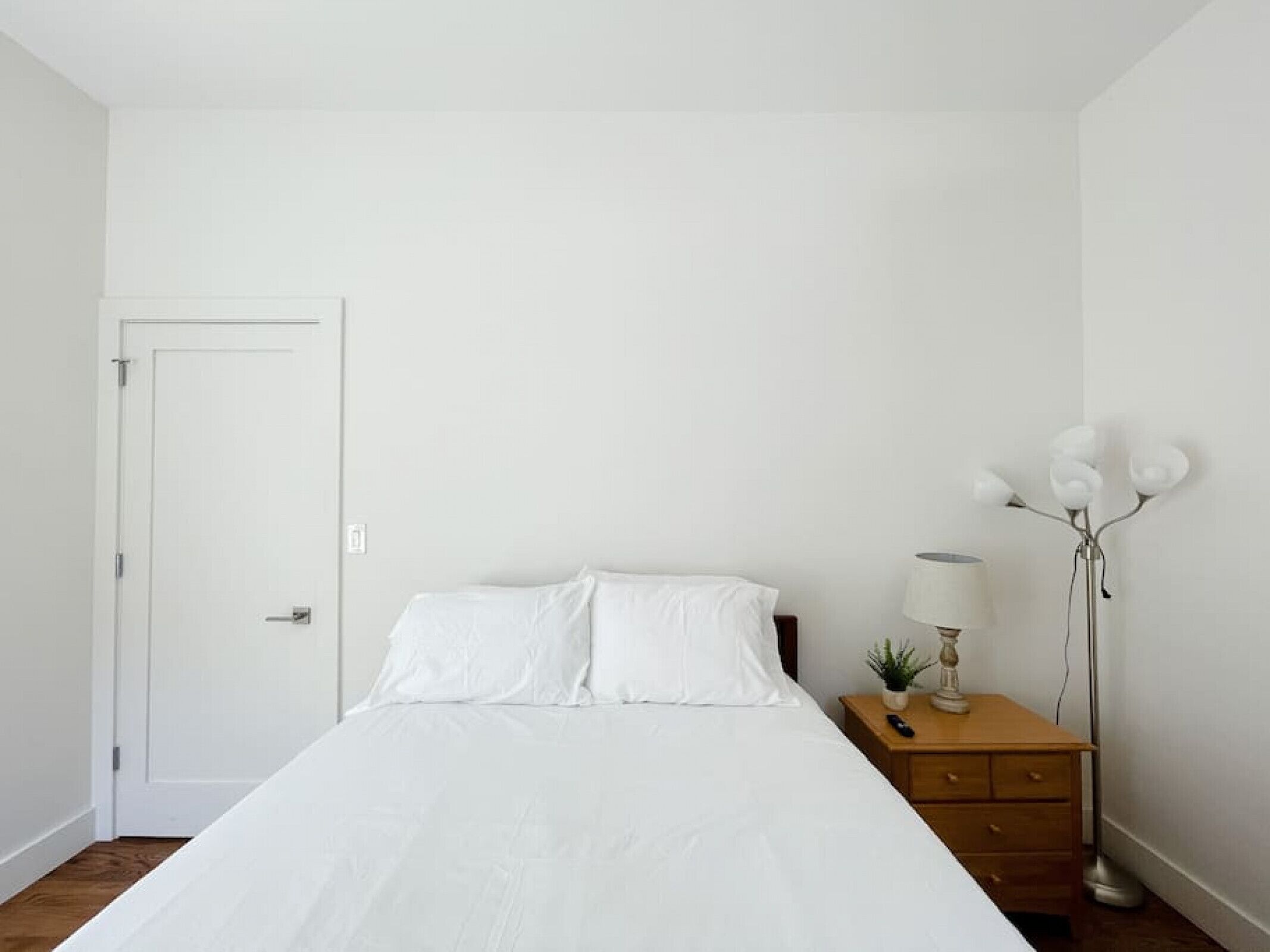 A bedroom with a bed, a wooden nightstand, a lamp, and a floor lamp.