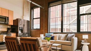 Una sala de estar moderna con un sofá, dos sillas de madera, una mesita de centro y vistas a la ciudad a través de amplios ventanales.
