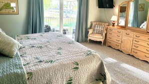 A bedroom with a bed, a chair, a dresser, a ceiling fan, a TV, and a balcony with curtains. - Perfect Naples golf and beach getaway! Just minutes from downtown and beaches. (Naples)