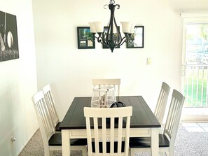 Een eetgedeelte met een donker houten tafel, witte stoelen, een kroonluchter en lijstwerken aan de muur.