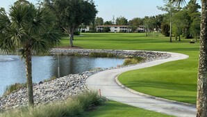 A golf course with a pond, a curved pathway, and a building in the background. - Perfect Naples golf and beach getaway! Just minutes from downtown and beaches. (Naples)