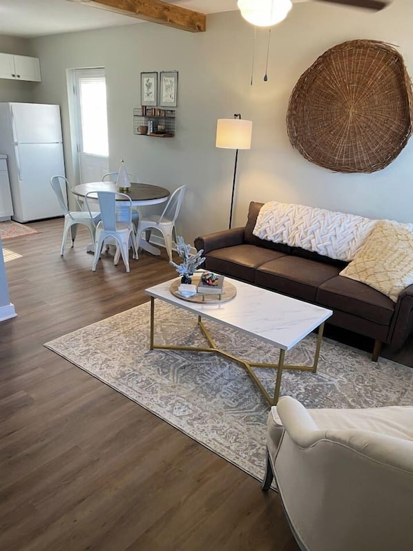 A living room with a brown sofa, a white coffee table, and a dining area with a round table and chairs.