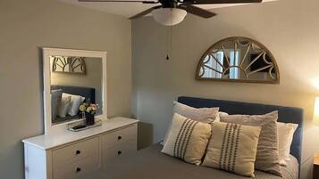 Een slaapkamer met een bed, een dressoir, een plafondventilator, een spiegel en een decoratief object aan de muur.