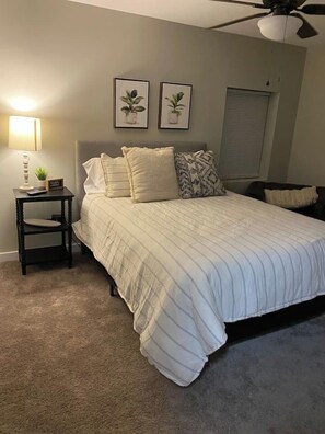 A bedroom with a bed, a nightstand, a lamp, and two framed pictures on the wall.
